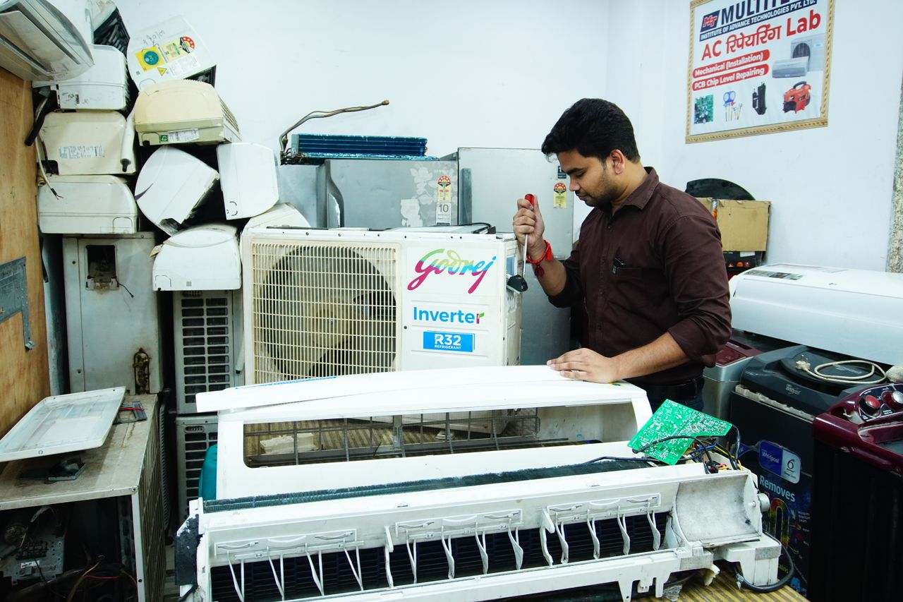 hero-img-02 Technician repairing an air conditioner unit in New Delhi workshop.